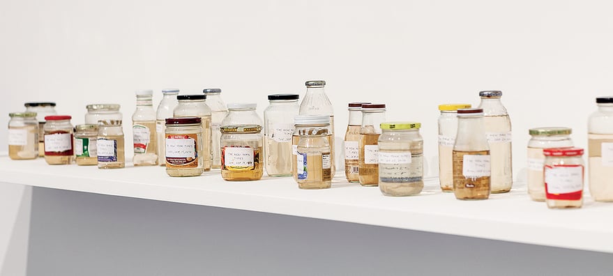Kirsten Pieroth, <em>Conversation Piece</em>, 2010. 30 jars, liquid from boiled newspapers, dimensions variable, shelf 30 × 270 cm. Courtesy the artist and Galleria Franco Noero, Torino. Photo credit: Andrew Curtis
