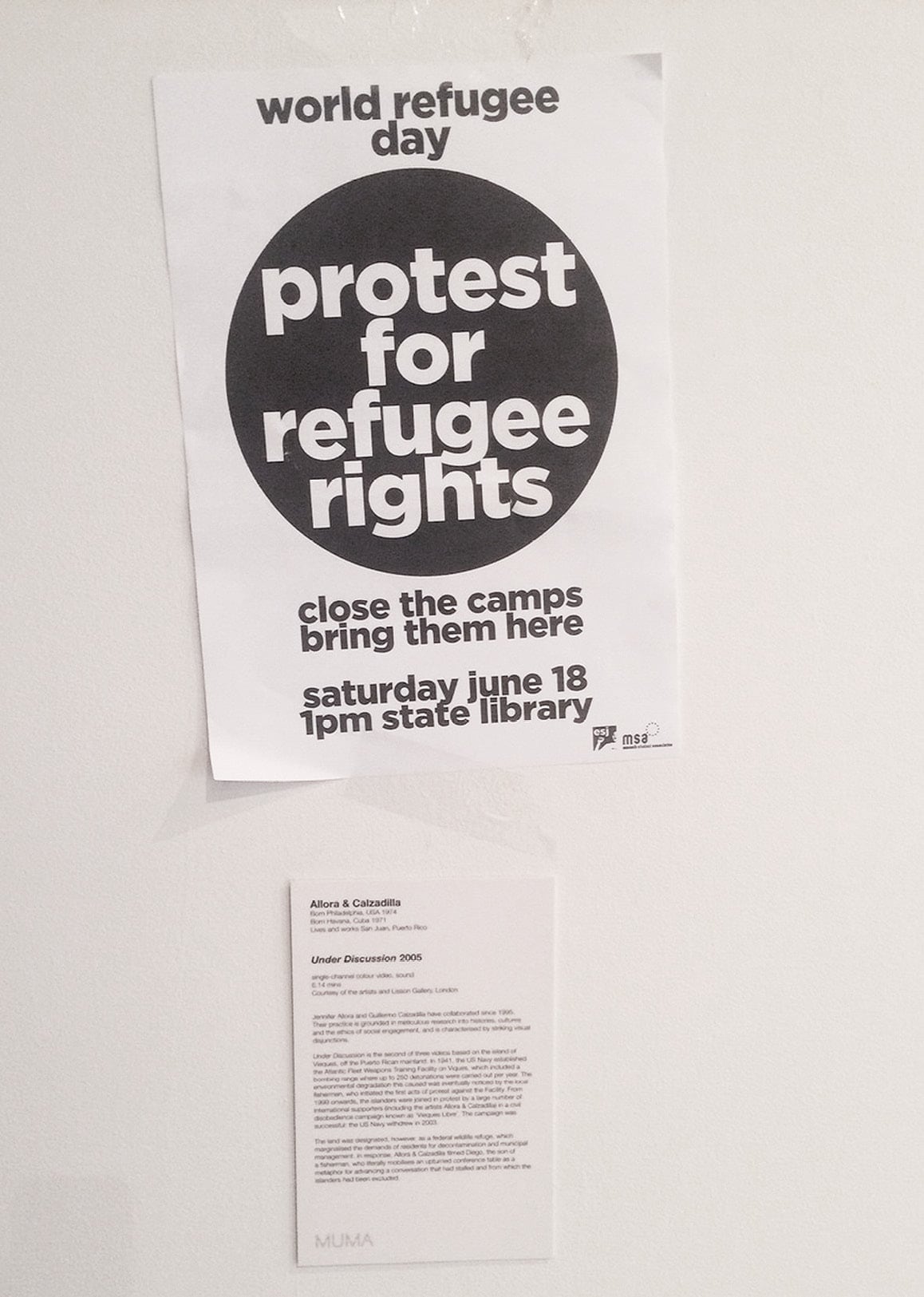 Photograph of flyer for protest left in <em>Borders, Barriers, Walls</em> above wall details for Amy Spiers and Catherine Ryan’s <em>The Least of the Doorkeepers (It is Possible but Not at the Moment)</em> 2016. Image courtesy Amy Spiers. Photo credit: Amy Spiers