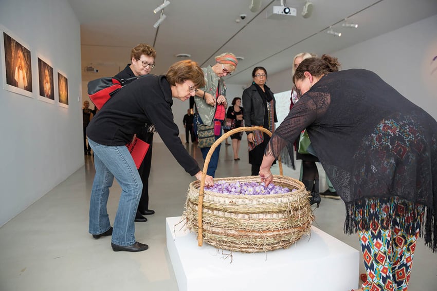 Visitors take purple poppies from a basket made by Aunty Phyllis Stewart, part of the remember (2016) installation by Genevieve Grieves for the With Secrecy and Despatch exhibition at Campbelltown Arts Centre.