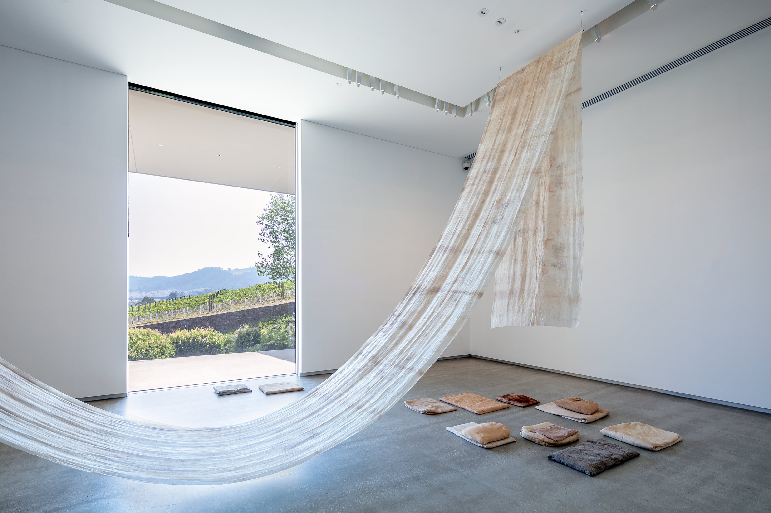 All images: Katie West, 'Clearing' (2018–19), suspended fabric: silk dyed with eucalyptus and wattles collected from area around Maroondah Dam; cushions: silk dyed with eucalyptus leaves and bark; muslin dyed with puff ball fungus; calico dyed with eucalyptus leaves and bark and puff ball fungus; all filled with wool and cotton wadding; sound: composed by Simon Charles with spoken score by Katie West, duration 00:13:00; texts: Kerry Arabena, Aunty Joy Murphy Wandin, Bruce Pascoe and Uncle David Wandin in partnership with Yarra Ranges Council, Dixon’s Creek Primary School, Ralph Hume, Victor Steffensen and Brett Ellis. Image courtesy of the artist. Photo credit: Andrew Curtis